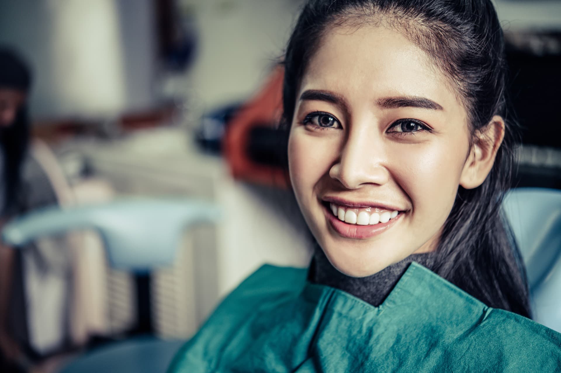 A smiling Malaysian patient seated comfortably in a bright dental chair